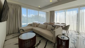 A modern living room with a sectional sofa, a glass coffee table, and a dining area with a round table and chairs. - 2BR Exclusive Private Pool • Canal view y Beach (Las Jarretaderas)