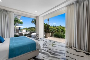 A modern hotel room with a bed, a balcony with a view of the outdoors, and a dining area.