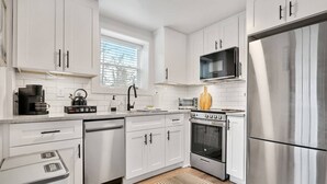 Une cuisine moderne avec des meubles blancs, des appareils en acier inoxydable, un four à micro-ondes, un grille-pain et un grand réfrigérateur.