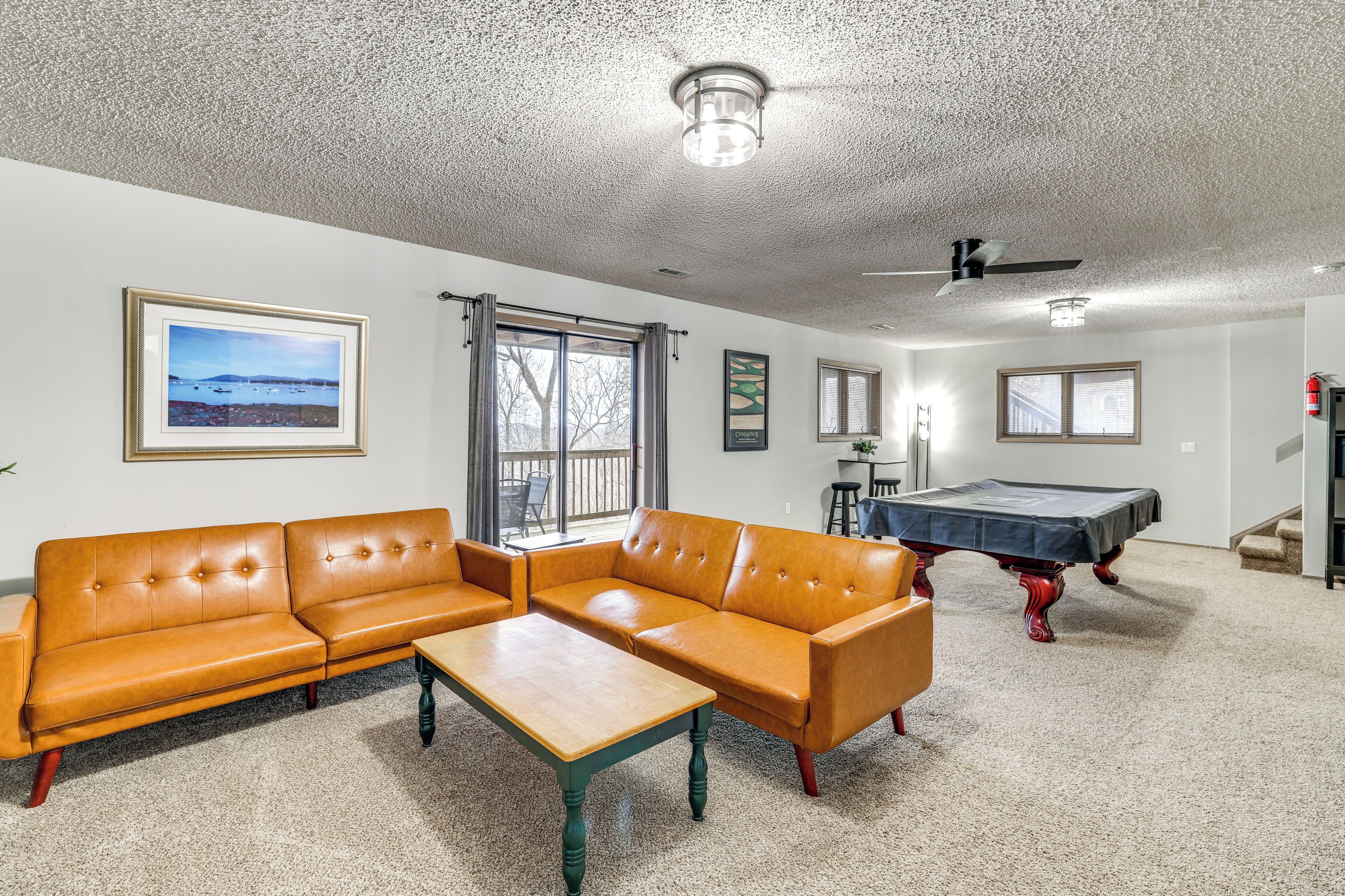 A living room with a sectional sofa, a coffee table, a pool table, and a view of the outdoors through large windows.
