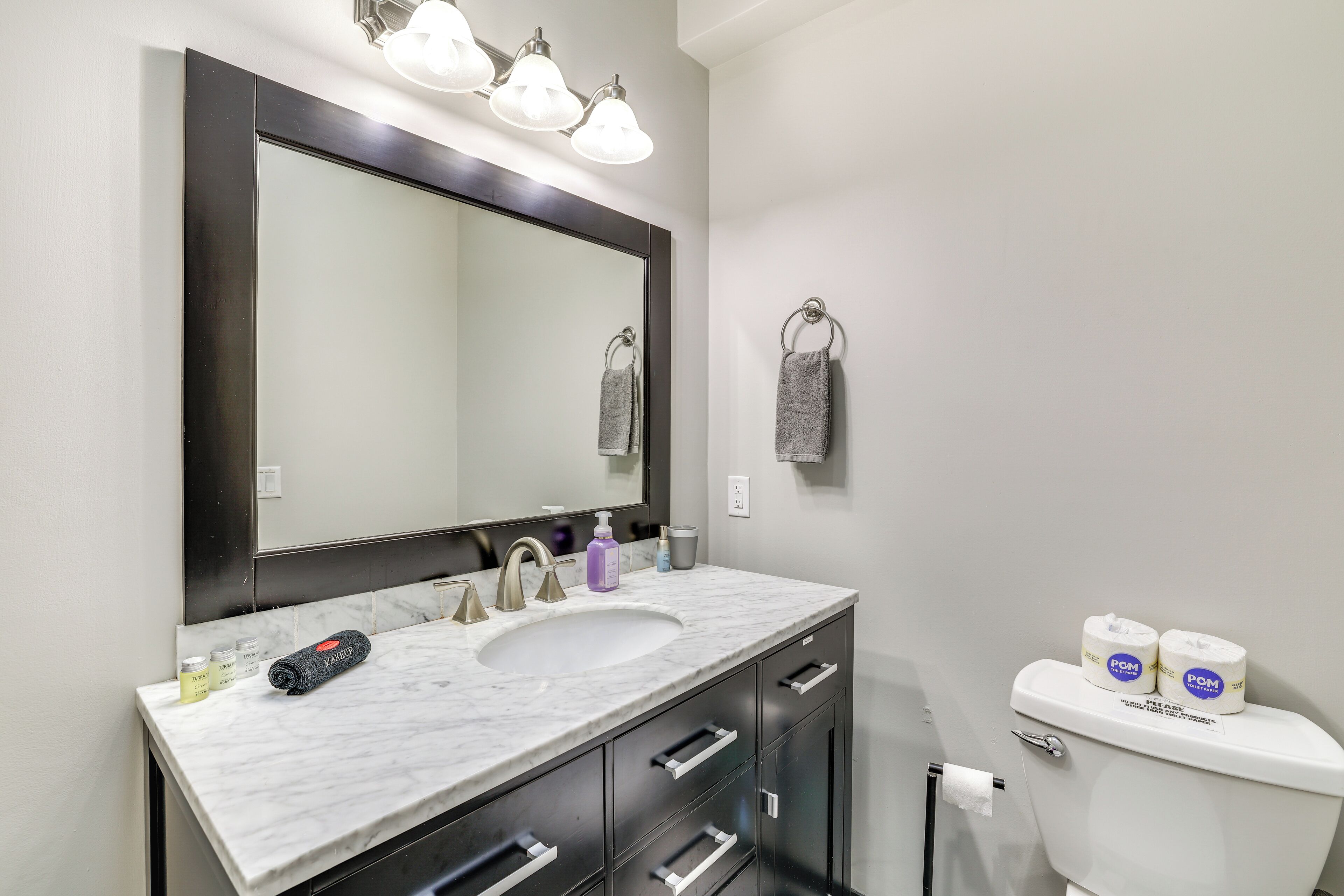 A bathroom with a marble sink, a large mirror, a towel ring, and two rolls of toilet paper.