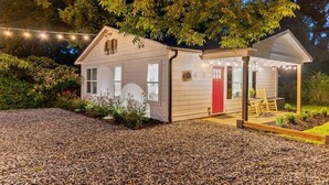 Una pequeña casa de una sola planta con puerta roja, un porche cubierto y luces colgantes.