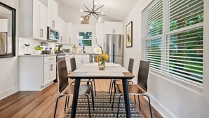 Una cocina moderna con armarios blancos, una isla central y un comedor con mesa y sillas.