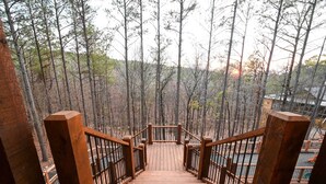Un escalier en bois descend vers une zone boisée, offrant une vue sur une étendue d’eau.