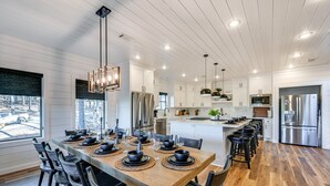 Une cuisine moderne avec des meubles blancs, des appareils en acier inoxydable et une table à manger en bois pour six personnes.