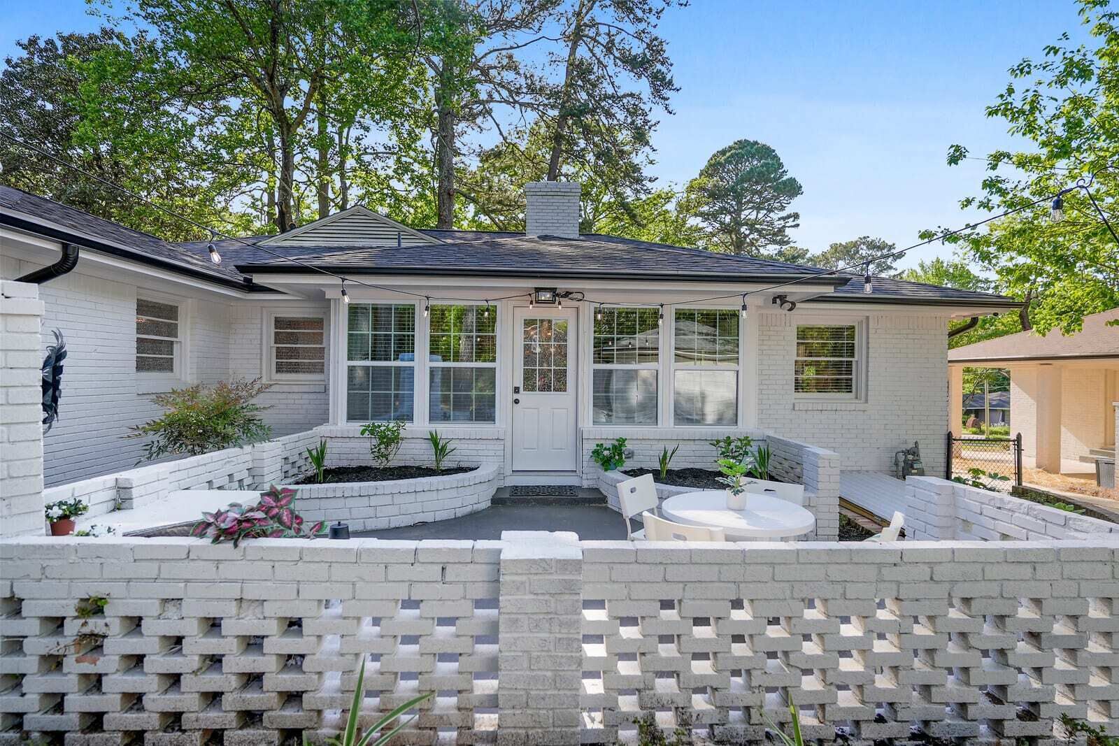 Ein Haus mit überdachter Terrasse, einer Backsteinmauer und einem kleinen Gartenbereich mit Blumentöpfen.