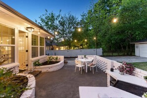 A patio area with a round table and chairs, a brick planter, and string lights. - Divine Digs | Luxury in a Hip Area (Atlanta)