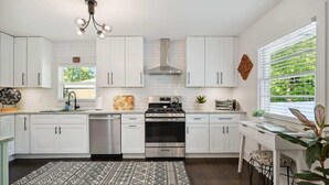 Una cocina moderna con armarios blancos, electrodomésticos de acero inoxidable, un tapete estampado y vistas a la vegetación exterior.