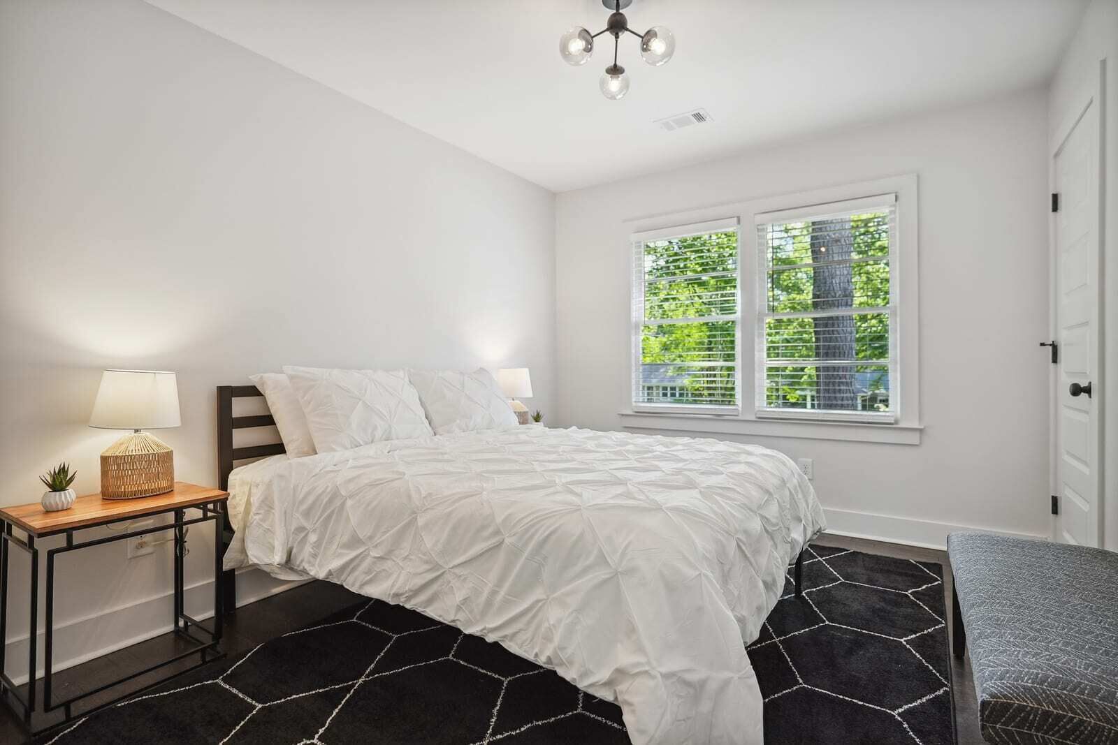 A bedroom with a bed, bedside tables, a lamp, a window with blinds, and a door.
