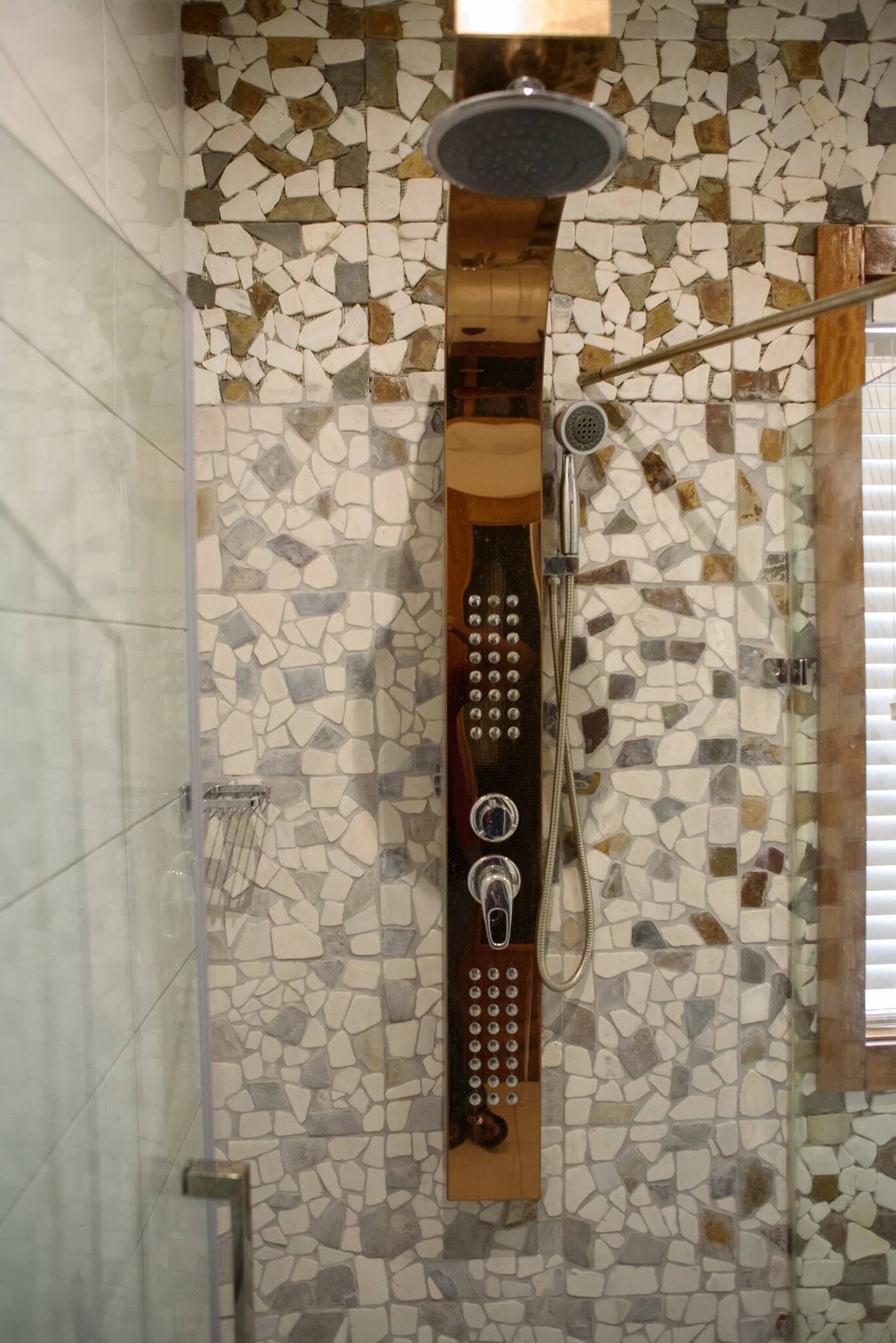 A shower with a mosaic wall, a handheld showerhead, and a control panel.