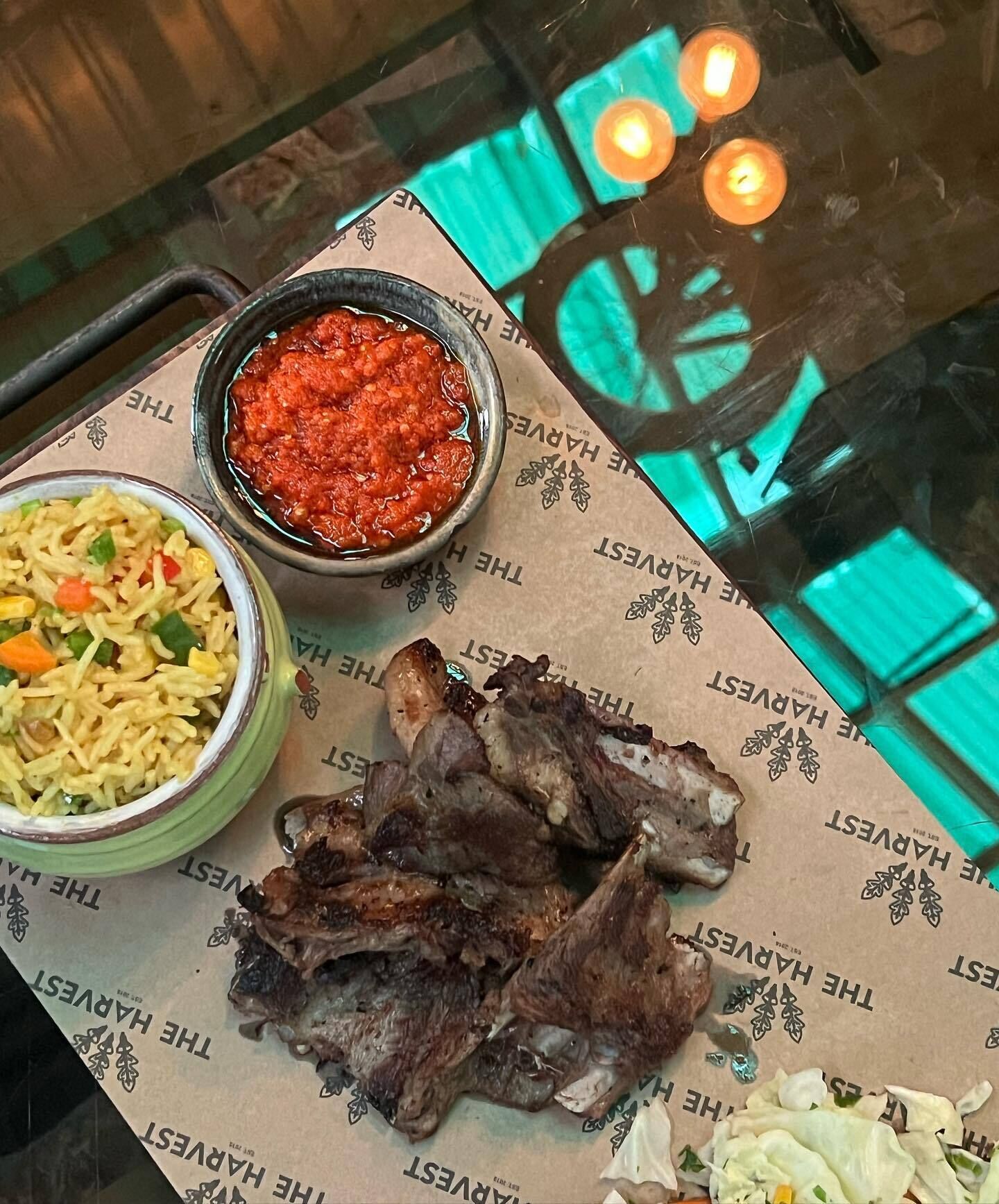Ein Tisch mit einer Mahlzeit aus gebratenem Reis, einer Schüssel rote Soße und gegrilltem Fleisch, darunter ein grün gemustertes Tischtuch.