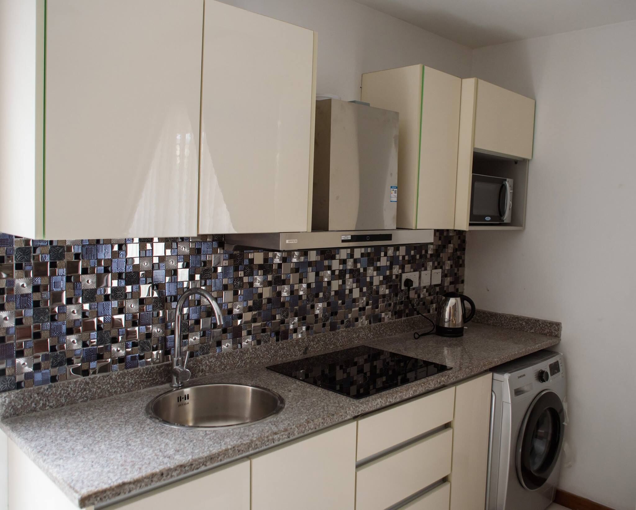 A kitchen with a stainless steel sink, a microwave, and a washing machine.