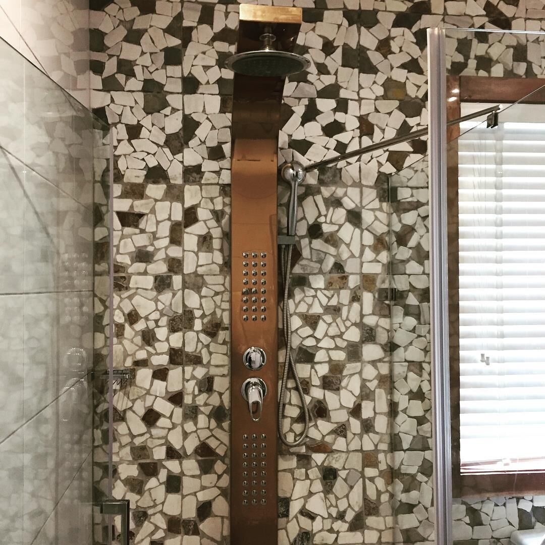 A shower with a mosaic tile wall, a glass enclosure, and a wooden panel above the showerhead.