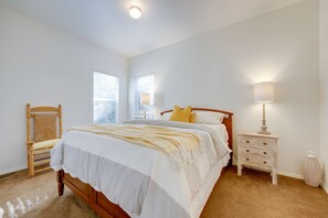 Un dormitorio con cama de madera, ropa de cama blanca, una mesita de noche con lámpara y una silla.