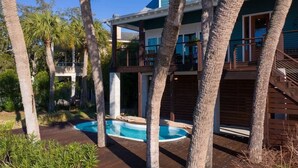 A two-story house with a swimming pool surrounded by palm trees.