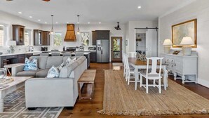A spacious living area with a sofa, dining table, and chairs, a kitchen with modern appliances, and a large window providing natural light.