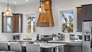A modern kitchen with wooden cabinets, stainless steel appliances, and a bar area with wicker chairs.