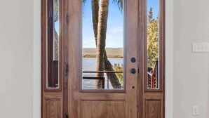 A wooden door with a glass panel and a view of a palm tree and water.