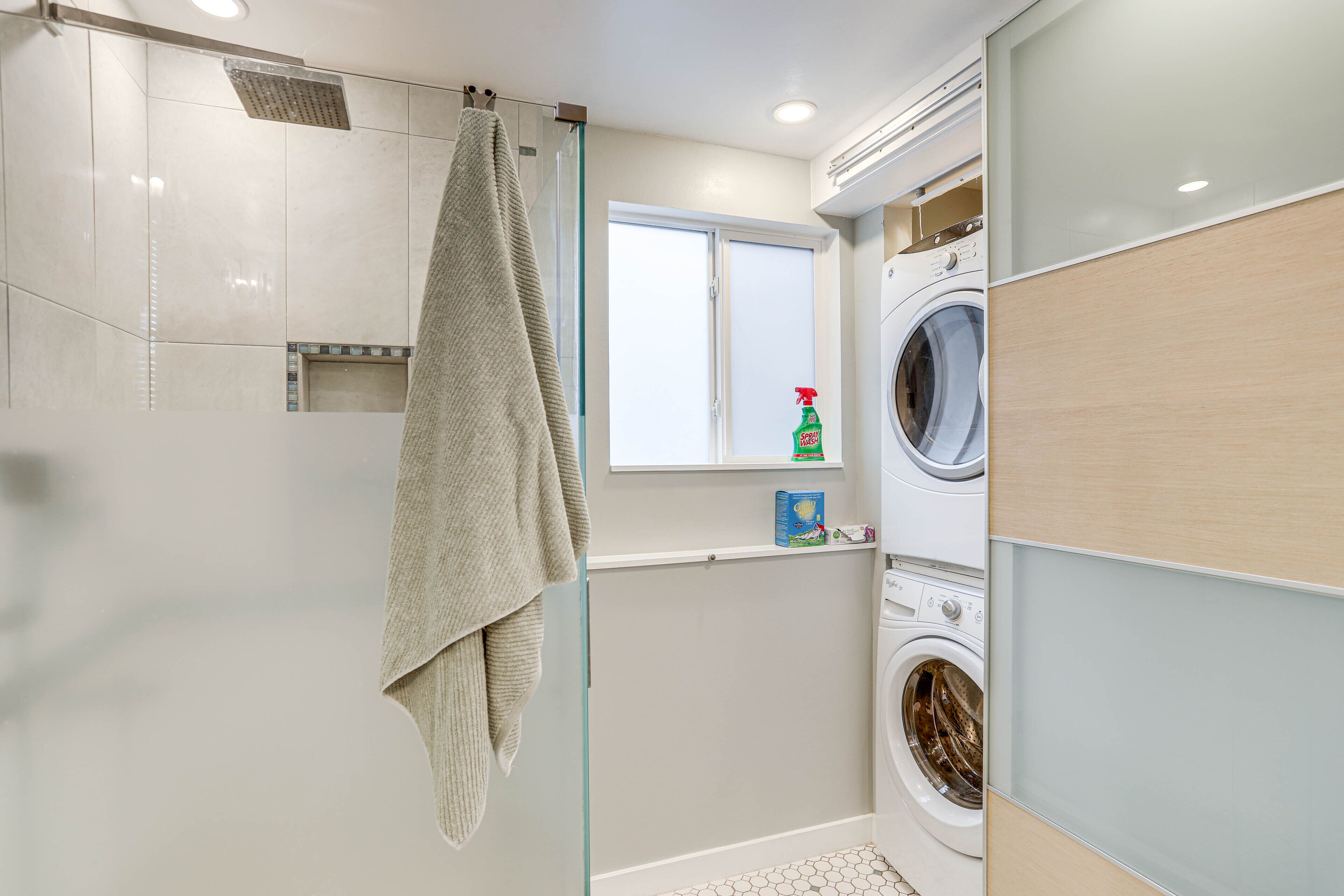 Une salle de bain moderne dotée d’une douche à parois de verre, d’un lave-linge encastré et d’une fenêtre offrant une vue agréable.