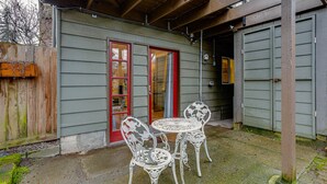 Une terrasse avec deux chaises en métal blanc et une table, une porte à cadre rouge et une clôture en bois.