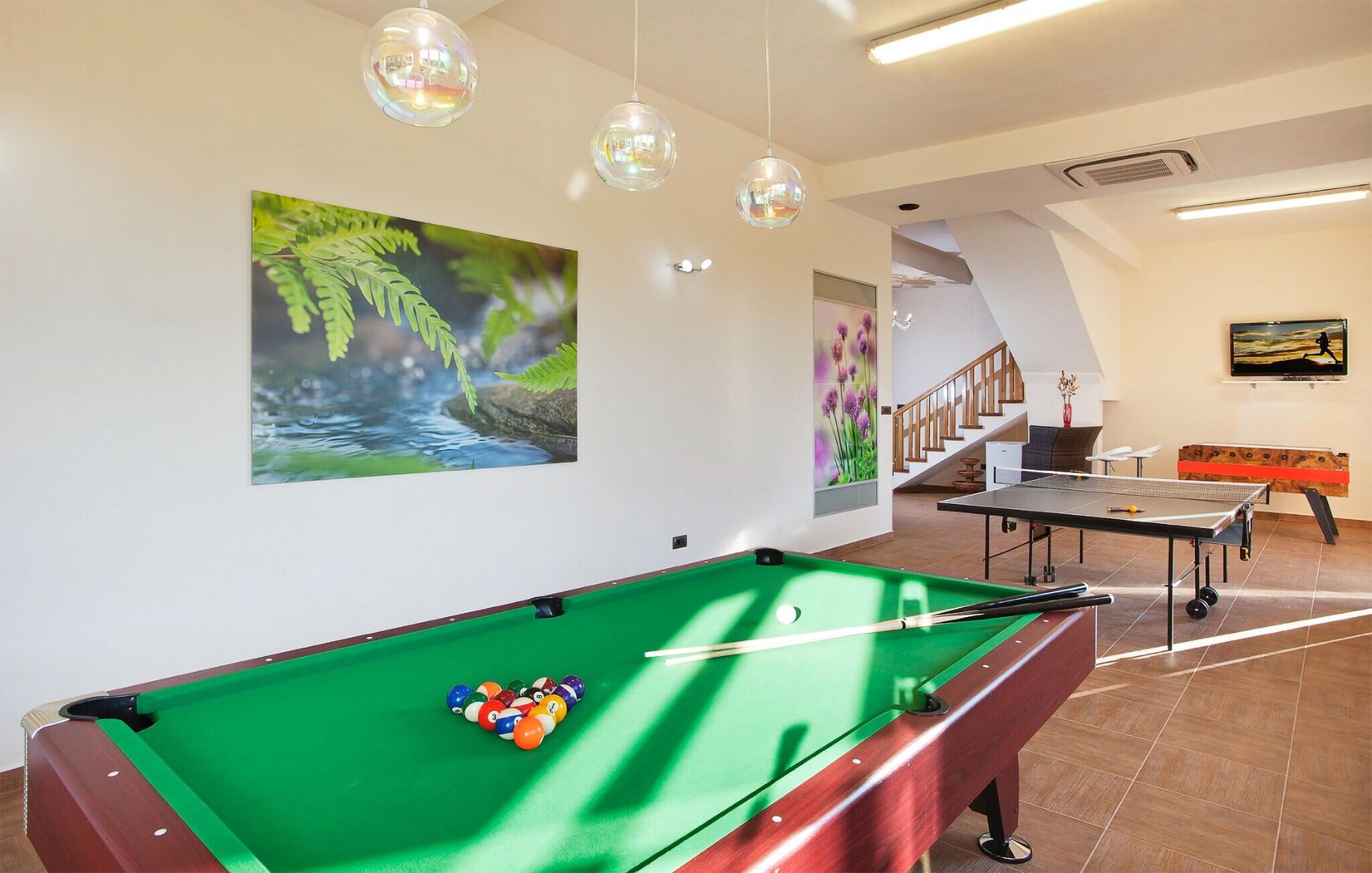 Une table de billard avec des billes, une table de ping-pong et un escalier menant à un balcon.