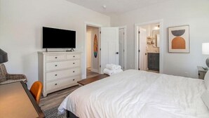 Ein Hotelzimmer mit einem großen Bett, einem Flachbildfernseher auf einer Kommode, einem Sessel und einem Bild an der Wand.