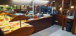 A buffet setup with various food items, a coffee machine, and a trash bin.