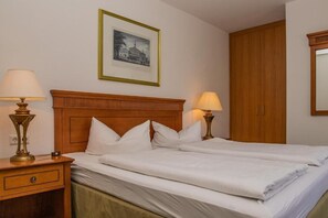 A hotel room with a wooden headboard, two beds, a nightstand with a lamp, a framed picture on the wall, and a wardrobe. - Alpenhotel Gastager (Inzell)