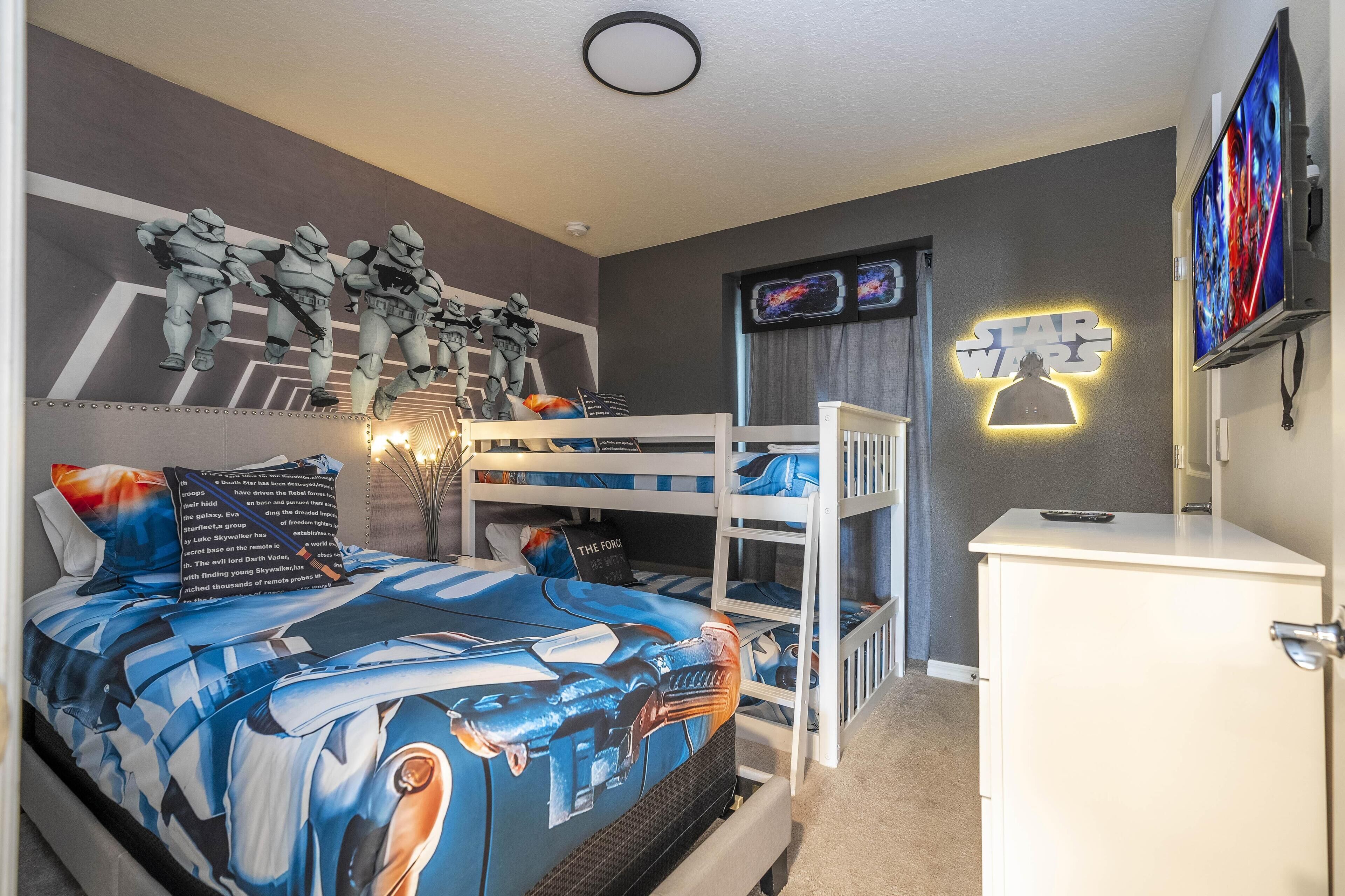 Un dormitorio con una colcha temática de Star Wars, literas y un cartel de Star Wars en la pared.