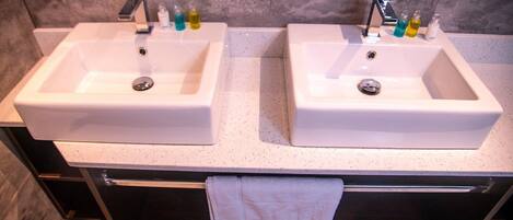 A bathroom with two white sinks, each with a faucet and soap dispensers. There is a towel hanging on a rack below the sinks.