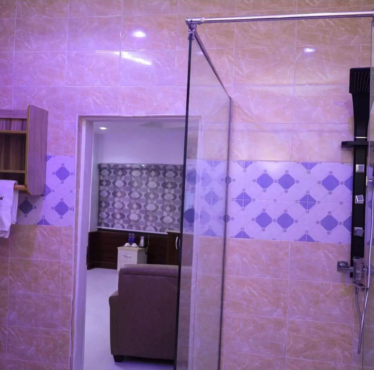 A bathroom with a glass shower enclosure, a towel rack, and patterned tiles.