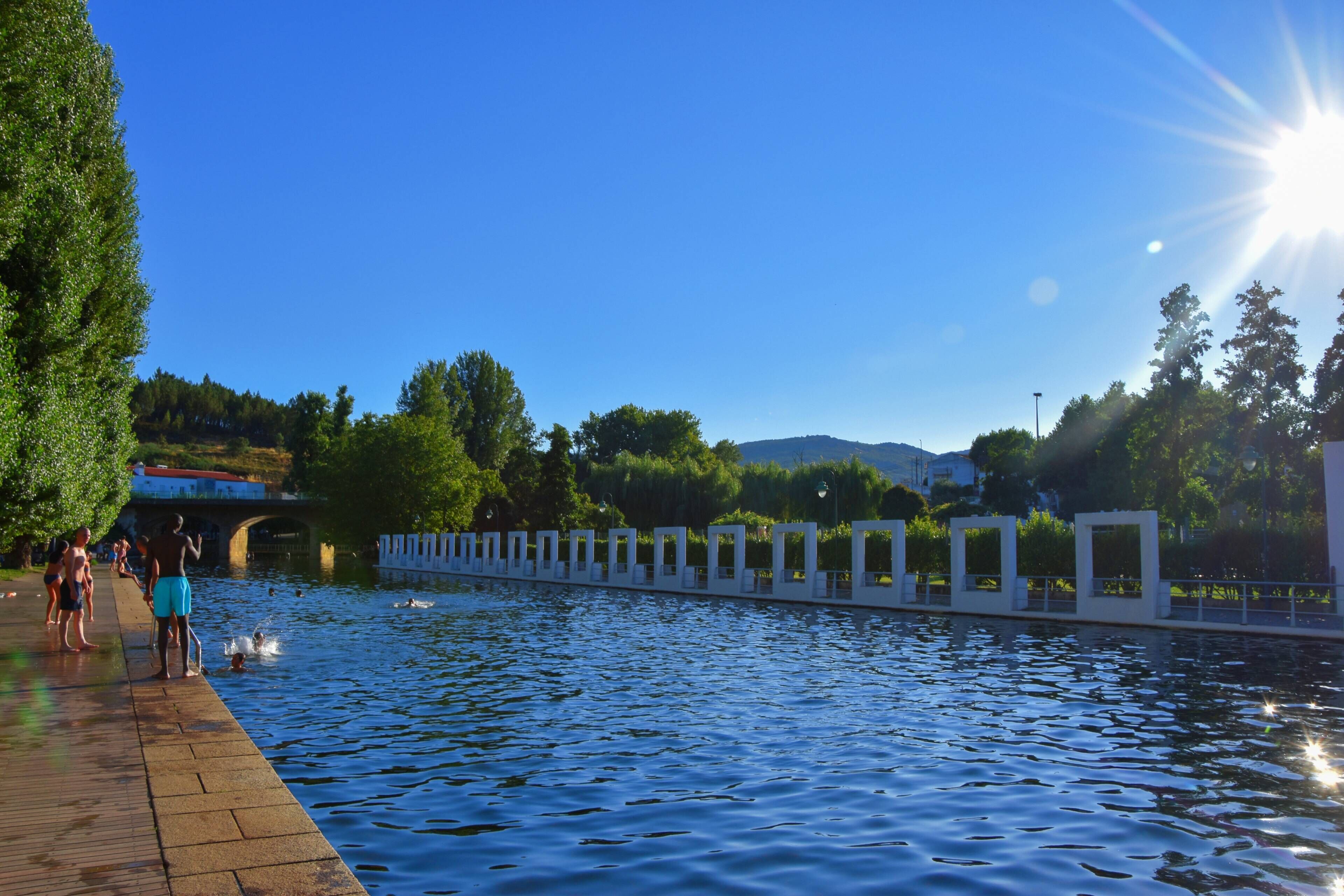 Un paseo ribereño con un puente al fondo, rodeado de follaje y árboles.