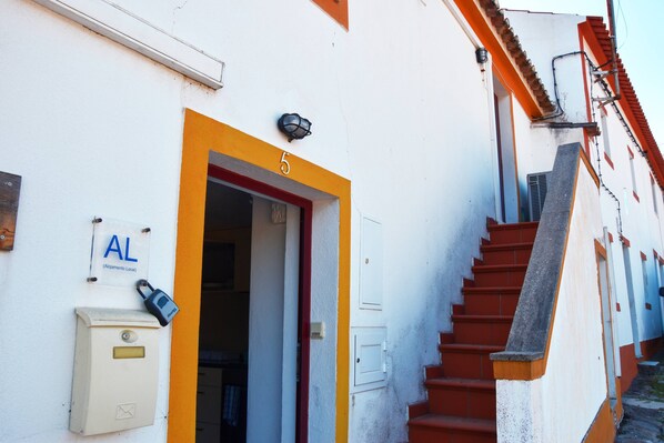 A building with a white facade, a red and yellow door, and a staircase leading to an upper level.
