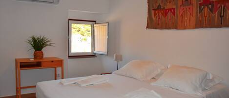 A bedroom with a bed, a nightstand, a lamp, a window, and a wall-mounted air conditioner.