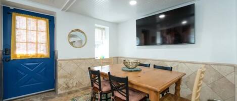A dining area with a wooden table, four chairs, a bowl, and a TV mounted on the wall.