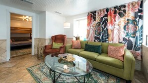 Ein Wohnzimmer mit einem grünen Sofa, einem Glastisch und einem gemusterten Vorhang.