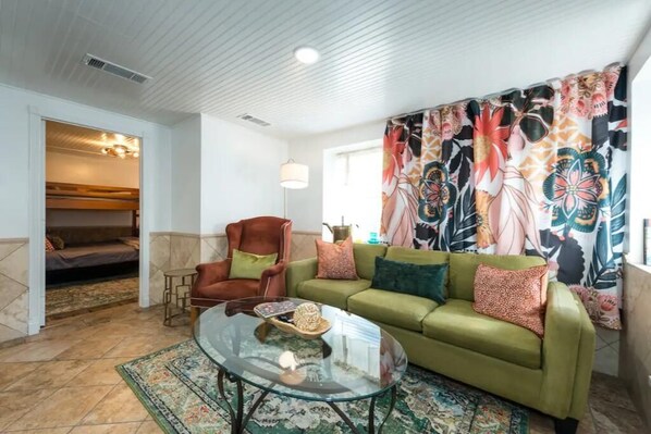 A living room with a green sofa, a glass coffee table, and a patterned curtain. - Hickory St. Lodge @ the square! (Denton)