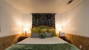 Ein ordentlich bezogenes Bett mit einem grün gemusterten Bettüberwurf, zwei Nachttischlampen und einer Wandteppich-Dekoration an der Wand.