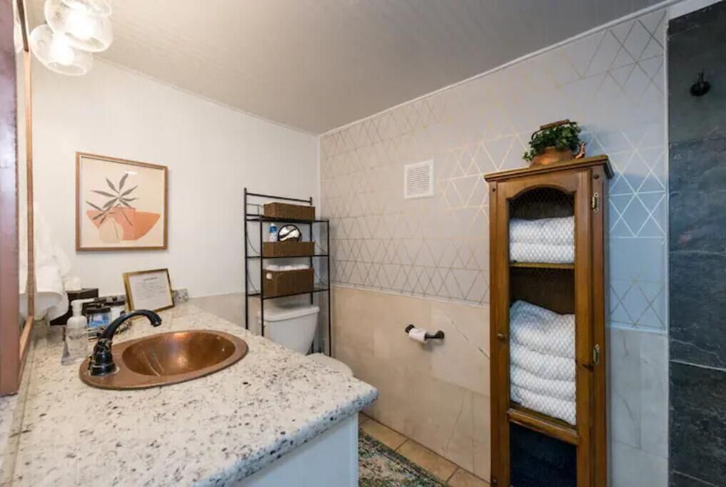Une salle de bain avec un lavabo doté d’un plan de travail en granit, un porte-serviettes, un tableau encadré et un mur orné d’un motif géométrique.