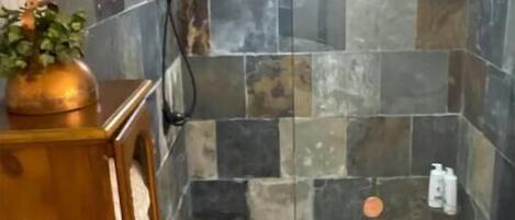 A shower area with stone tiles and a wooden cabinet with a plant.