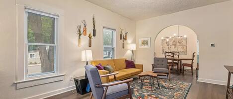 A spacious living room with a sofa, armchairs, a dining table, and a patterned rug.