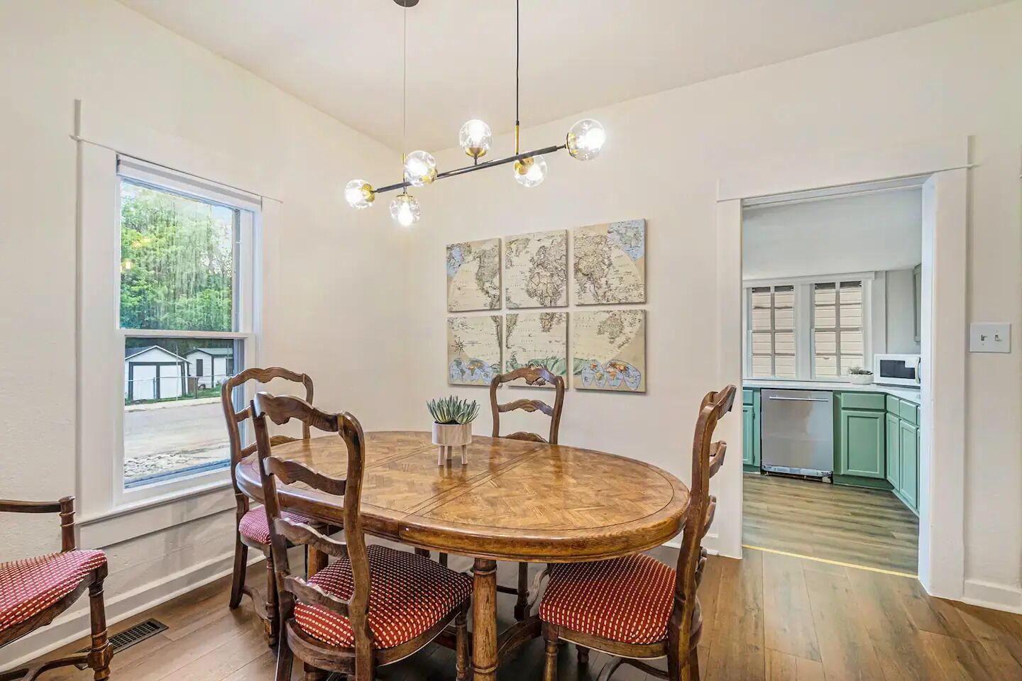A dining area with a wooden table and chairs, a chandelier, and a view of the outside.