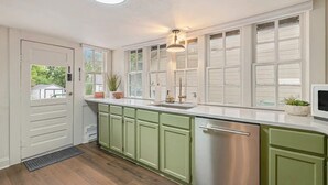 A kitchen with green cabinets, a stainless steel dishwasher, and a window with a view of greenery. - Downtown Loveland Bungalow, charming, historic 2BR recently remodeled gem. 

 (Loveland)
