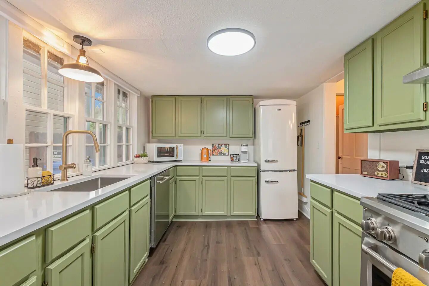 Une cuisine avec des meubles de couleur verte, un réfrigérateur blanc, un four à micro-ondes et une cuisinière.