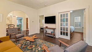 A spacious living room with a large TV, wooden furniture, and a patterned rug. - Downtown Loveland Bungalow, charming, historic 2BR recently remodeled gem. 

 (Loveland)