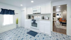 A modern kitchen with white cabinets, a built-in microwave, and a stove. There is a window with a dark valance and a potted plant. - Industrial St. Loft on the square (Denton)