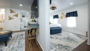 A modern living room with a blue sofa, a coffee table, and a TV mounted on the wall. There is a dining area with a table and chairs, and a kitchen in the background. - Industrial St. Loft on the square (Denton)