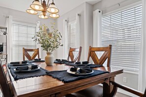 A dining area with a table for four, featuring a vase with a plant and matching chairs.