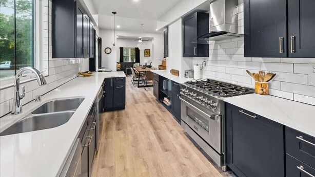 Una cucina moderna con mobili scuri, un piano di lavoro bianco e un'isola centrale.