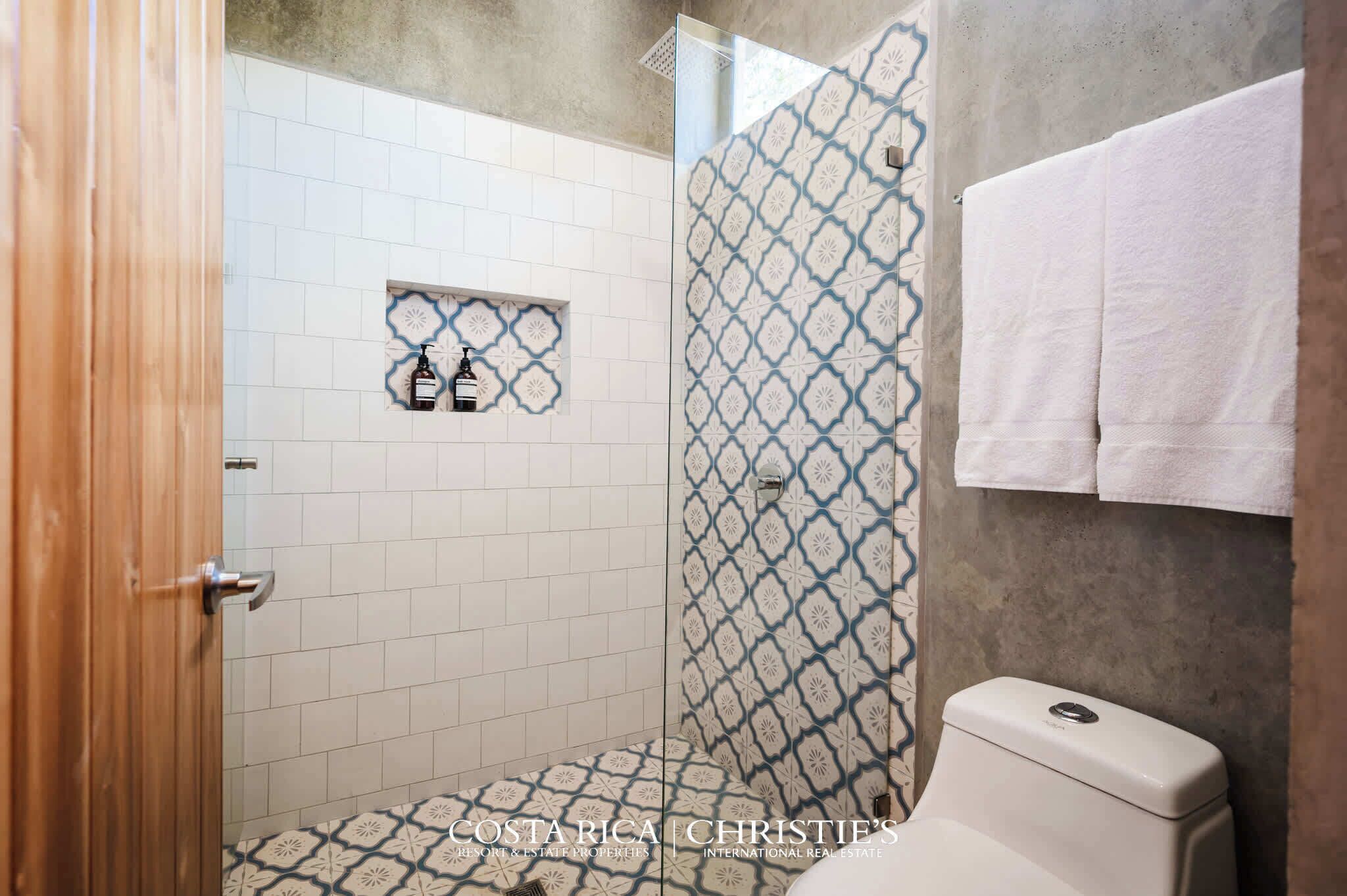 Un baño con ducha, inodoro y lavamanos con un rebozo de azulejos estampados.